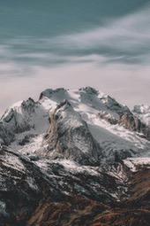 The summit of the snowy mountain is covered in white snow, the slopes are dotted with green vegetation, the sky is a bright blue, and the clouds float like cotton candy. - free wallpaper image