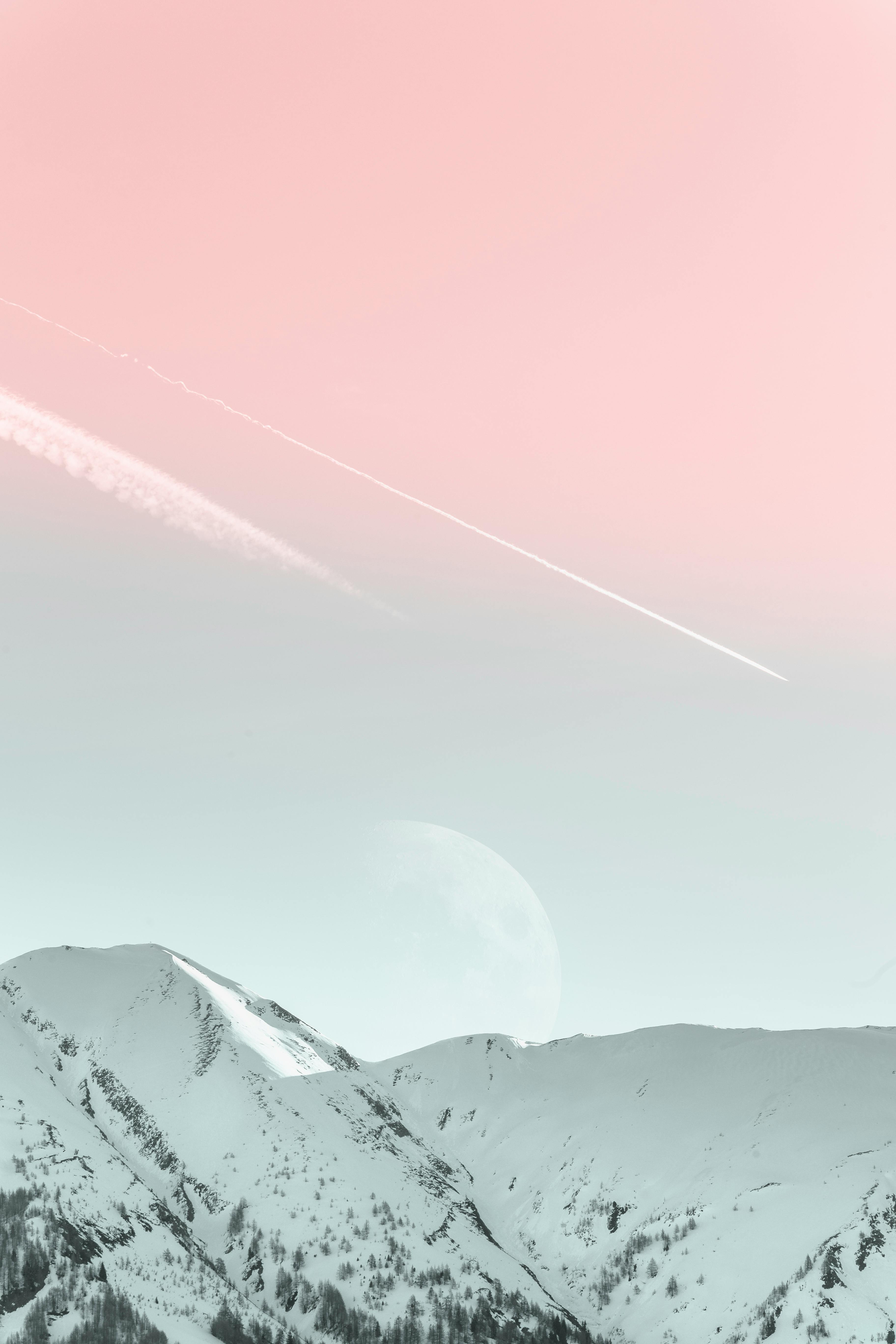 Snowy mountain peaks, pink sky with moon and contrails - free wallpaper image