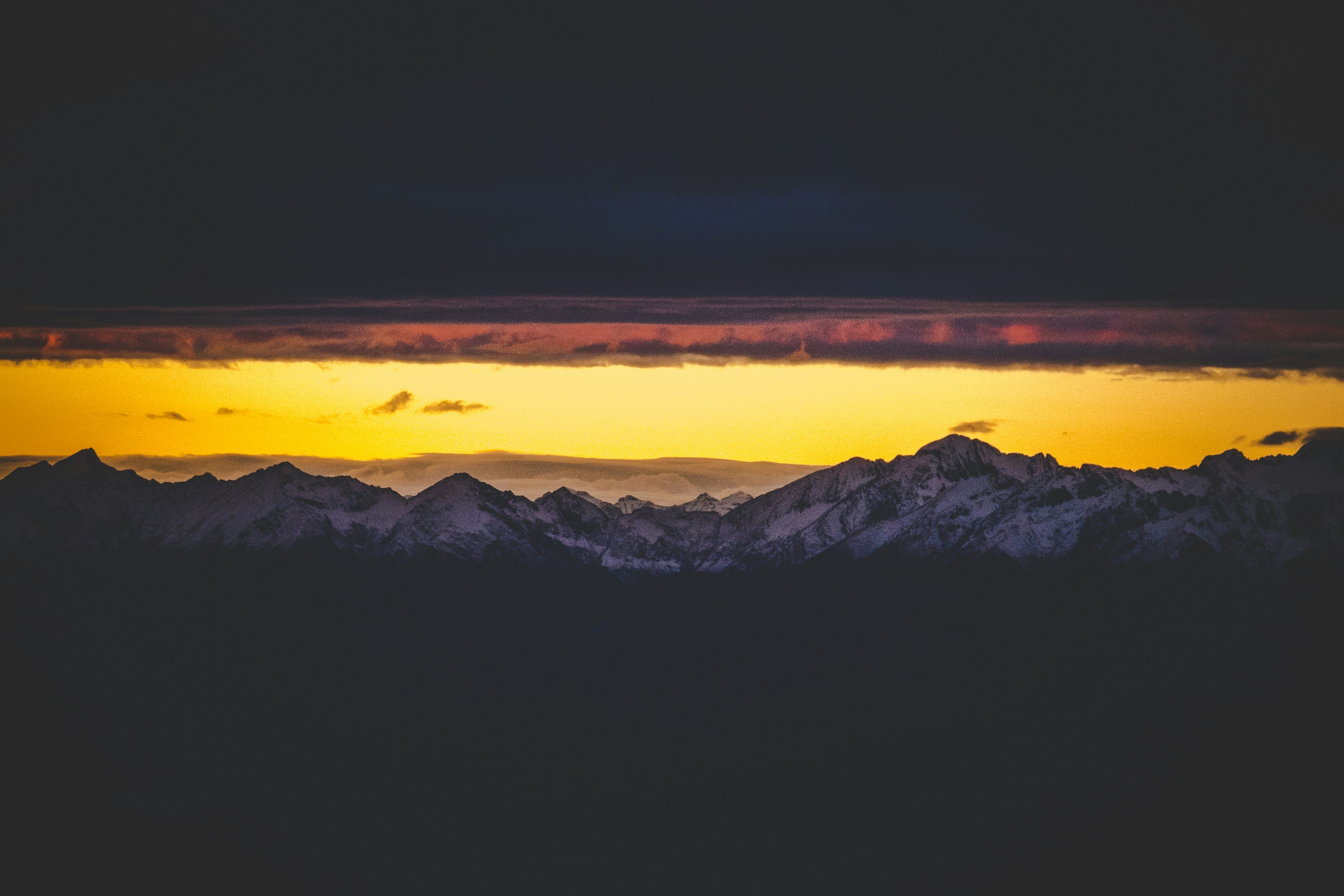 The sun is setting, clouds cover most of the sky, and the silhouette of the mountains is visible in the golden afterglow. - free wallpaper image