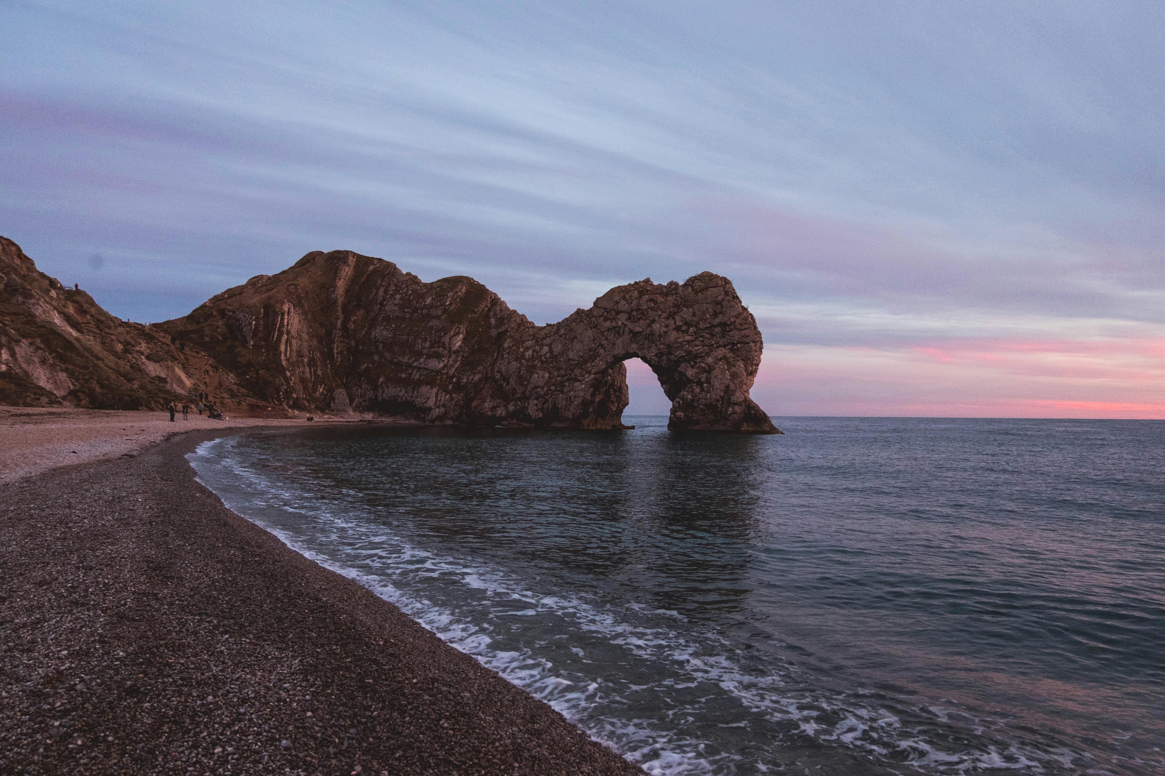 A sunset over the sea with a rocky arch in the foreground. The sky is a mix of orange and pink. - free wallpaper image