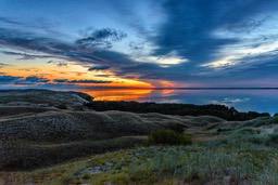 The sun sets in the distance, the sky is full of clouds, and there is a calm lake in the distance, with a green grassy field by the lake. - free wallpaper image