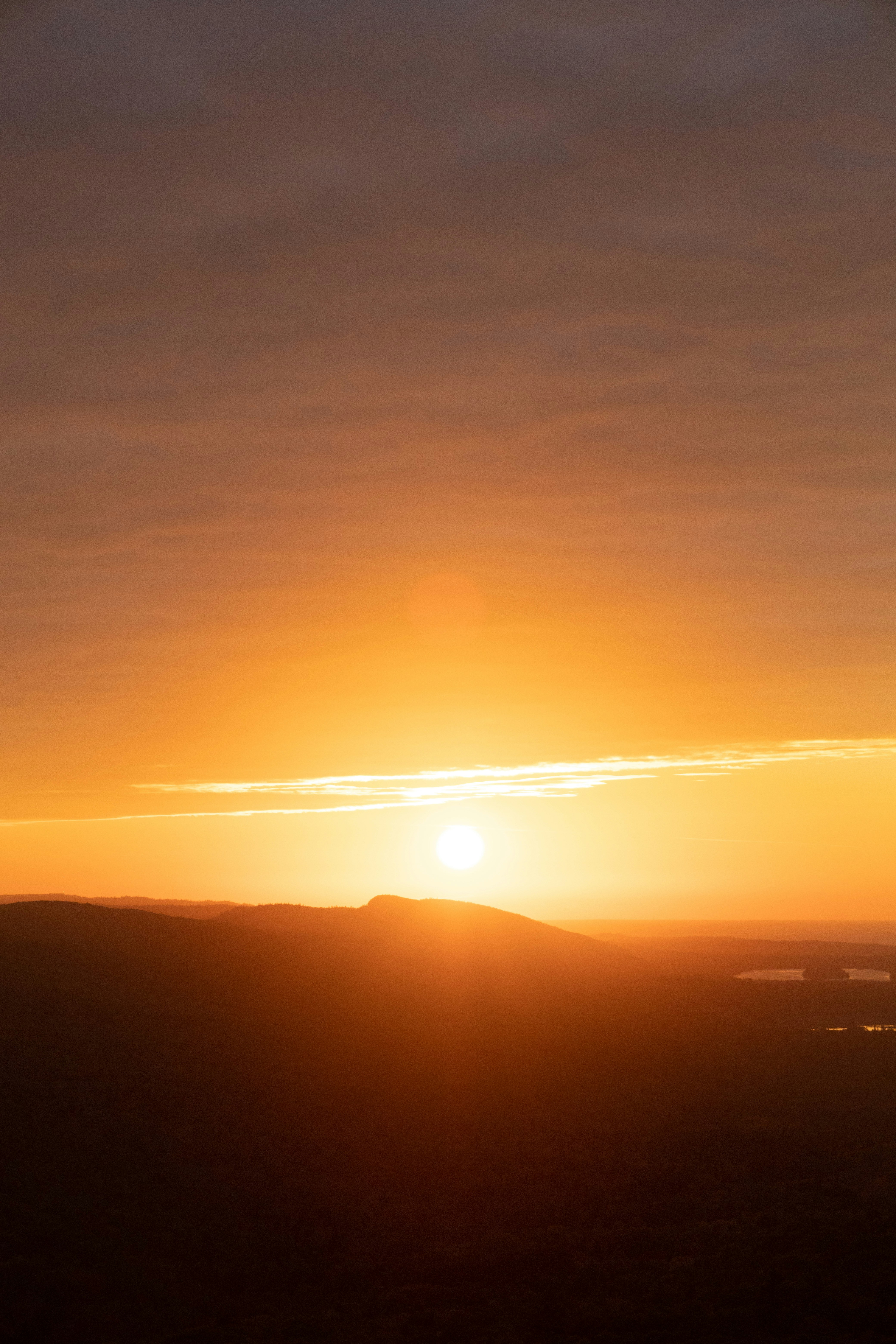 The sun sets over a landscape of rolling hills, the sky is filled with clouds. - free wallpaper image