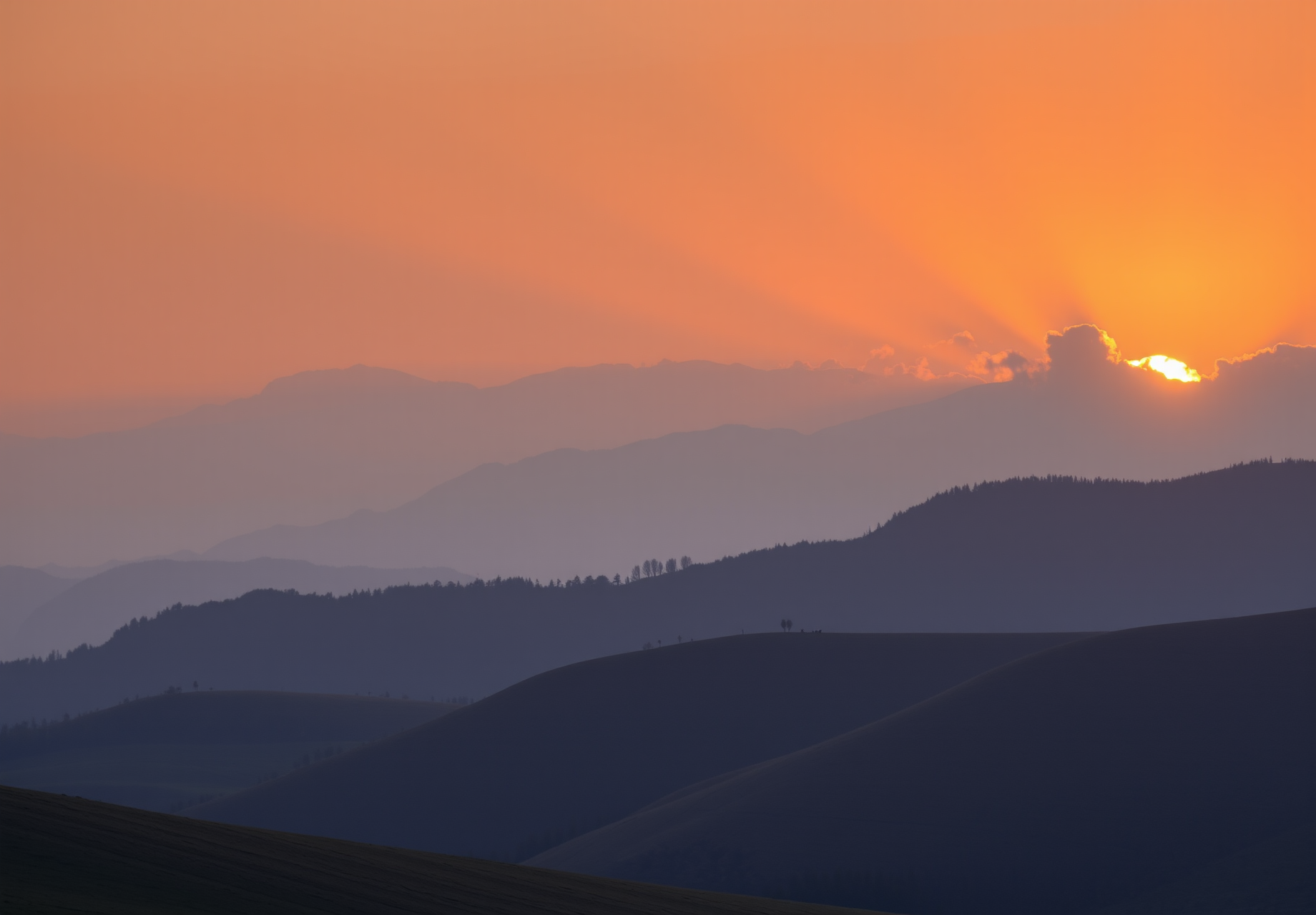 The sun sets over the mountains, casting a golden glow on the rolling hills. The mountains are shrouded in mist, creating a magnificent view. - wallpaper image