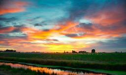 The sky is painted orange and blue as the sun sets, there is a river in the distance with green grass along the banks. - free wallpaper image