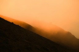 A mountain top is shrouded in fog, the sky is a warm orange. - free wallpaper image