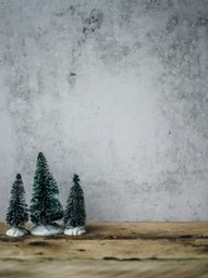 Three small Christmas trees are placed on a wooden floor, with a gray wall in the background. - wallpaper image