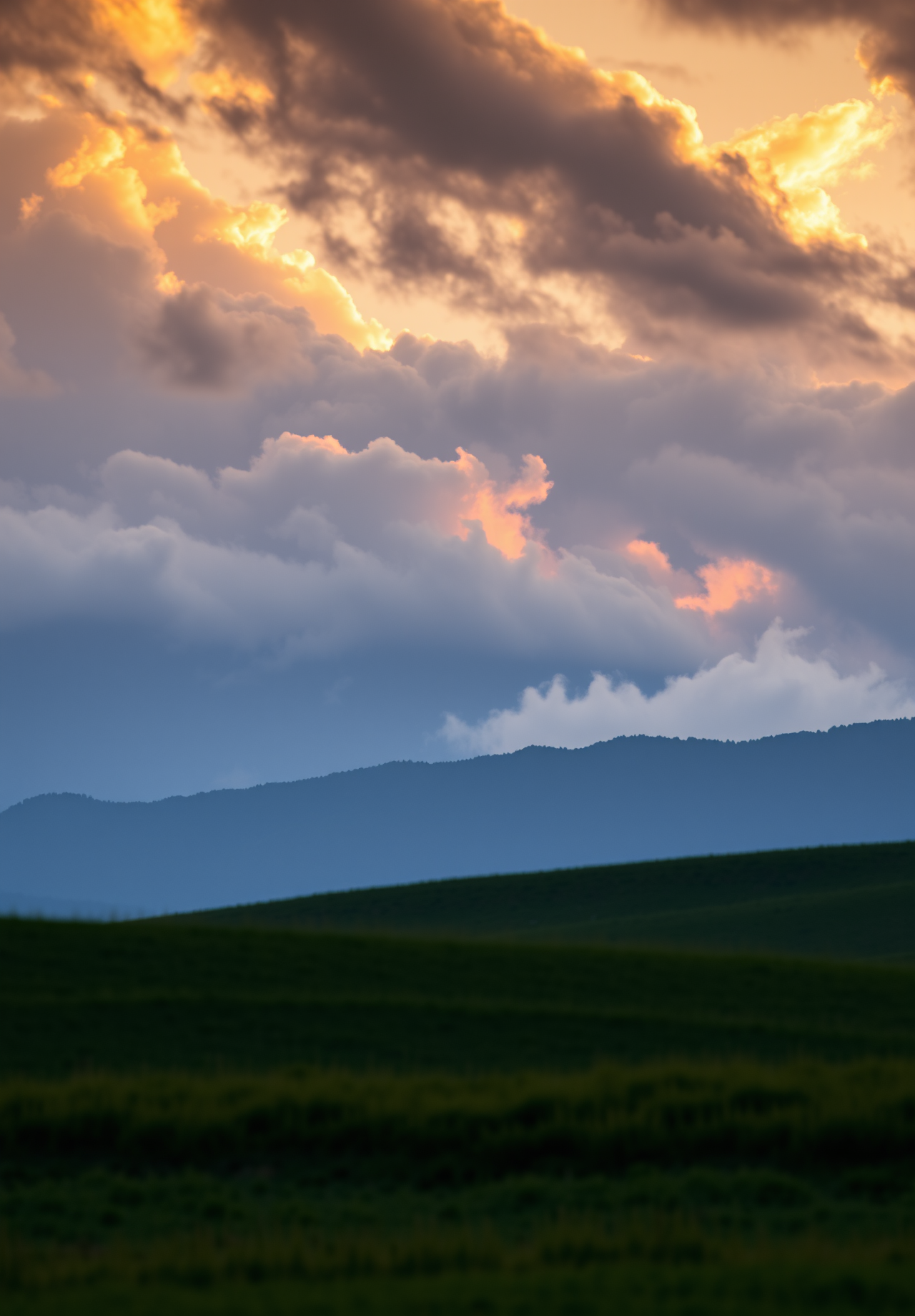 The sky is dyed orange by the sunset, with rolling hills and vast fields in the distance. - wallpaper image