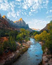 A winding river flows through a valley with towering rock formations and lush trees on either side, the sky is a clear blue with white clouds. - free wallpaper image