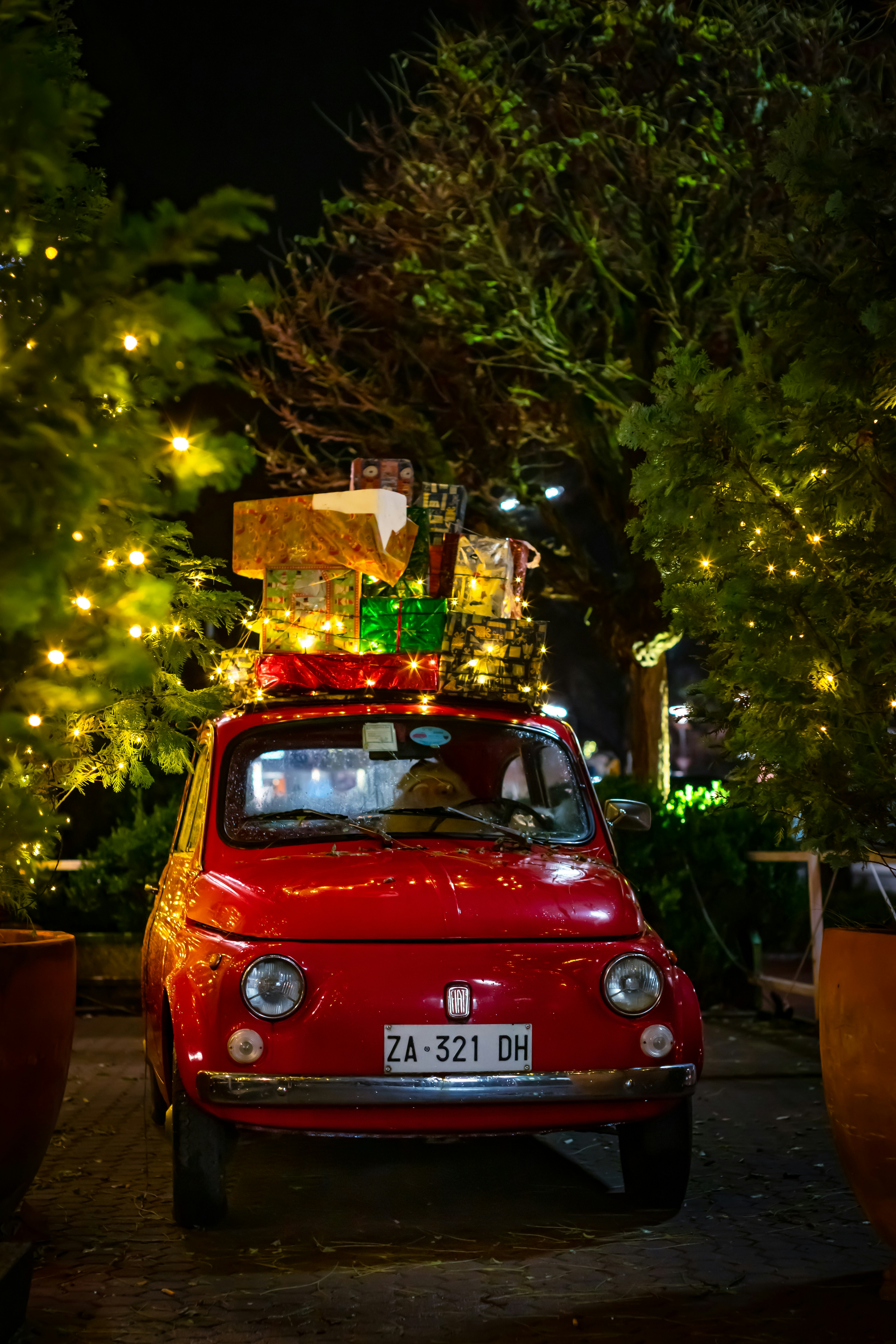 A red vintage car with Christmas presents piled on top, decorated with a Christmas tree beside it. - wallpaper image