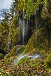 A rocky cliff covered in green moss with a waterfall cascading down the side, creating a breathtaking scene. - free wallpaper image