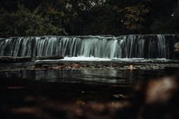 A waterfall cascades down from a height, the water rushing rapidly, surrounded by dense forest. - free wallpaper image