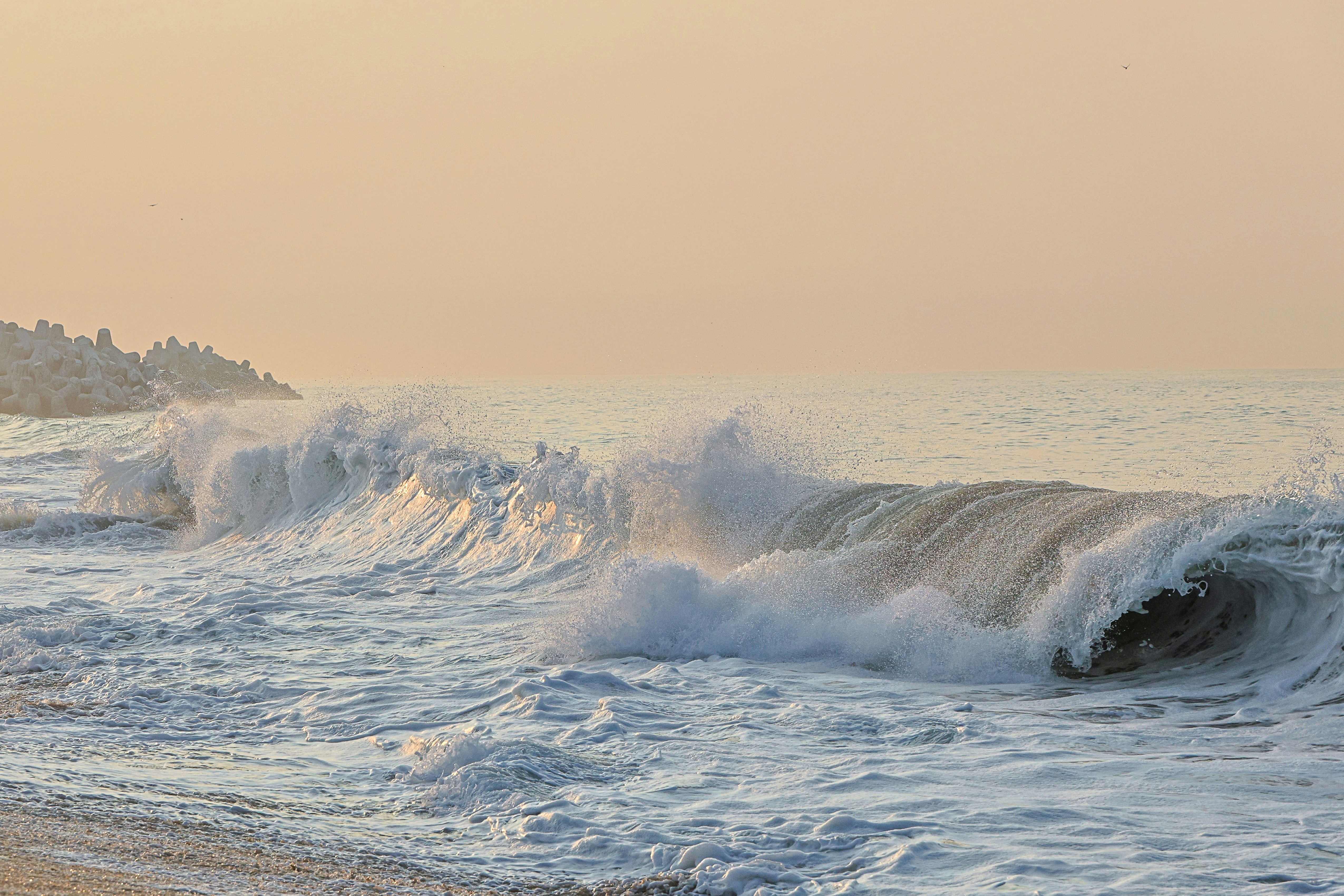 Waves crashing on the shore, creating white foam, with an orange glow in the sky, depicting a magnificent sunrise scene. - free wallpaper image