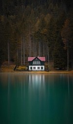 A white house sits by the lake, surrounded by a dense forest. - free wallpaper image