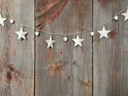 A garland of stars and bells is hanging on a wooden background, the stars are white and the bells are silver. - wallpaper image