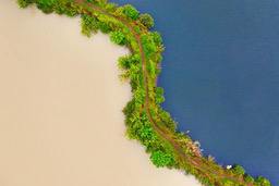 An aerial view of a winding path surrounded by green trees, separating a light-colored lake from a dark-colored lake. - free wallpaper image