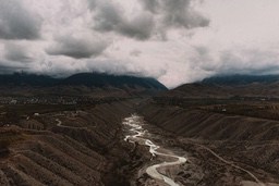 An aerial view of a winding river flowing through a valley with rolling hills on either side, the sky is overcast. - free wallpaper image