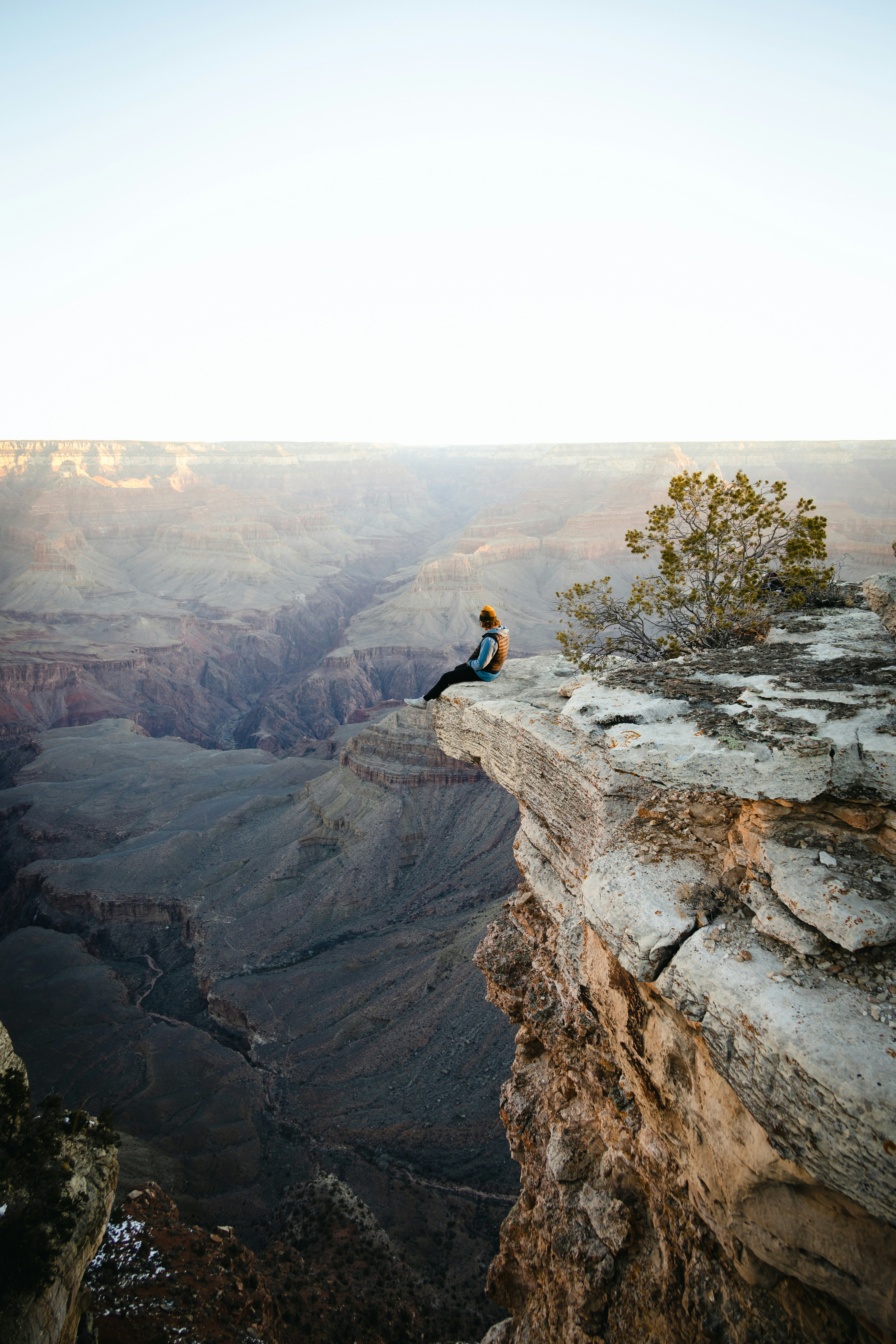 A woman sits on the edge of a cliff overlooking a majestic canyon. - free wallpaper image