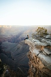 A woman sits on the edge of a cliff overlooking a majestic canyon. - free wallpaper image