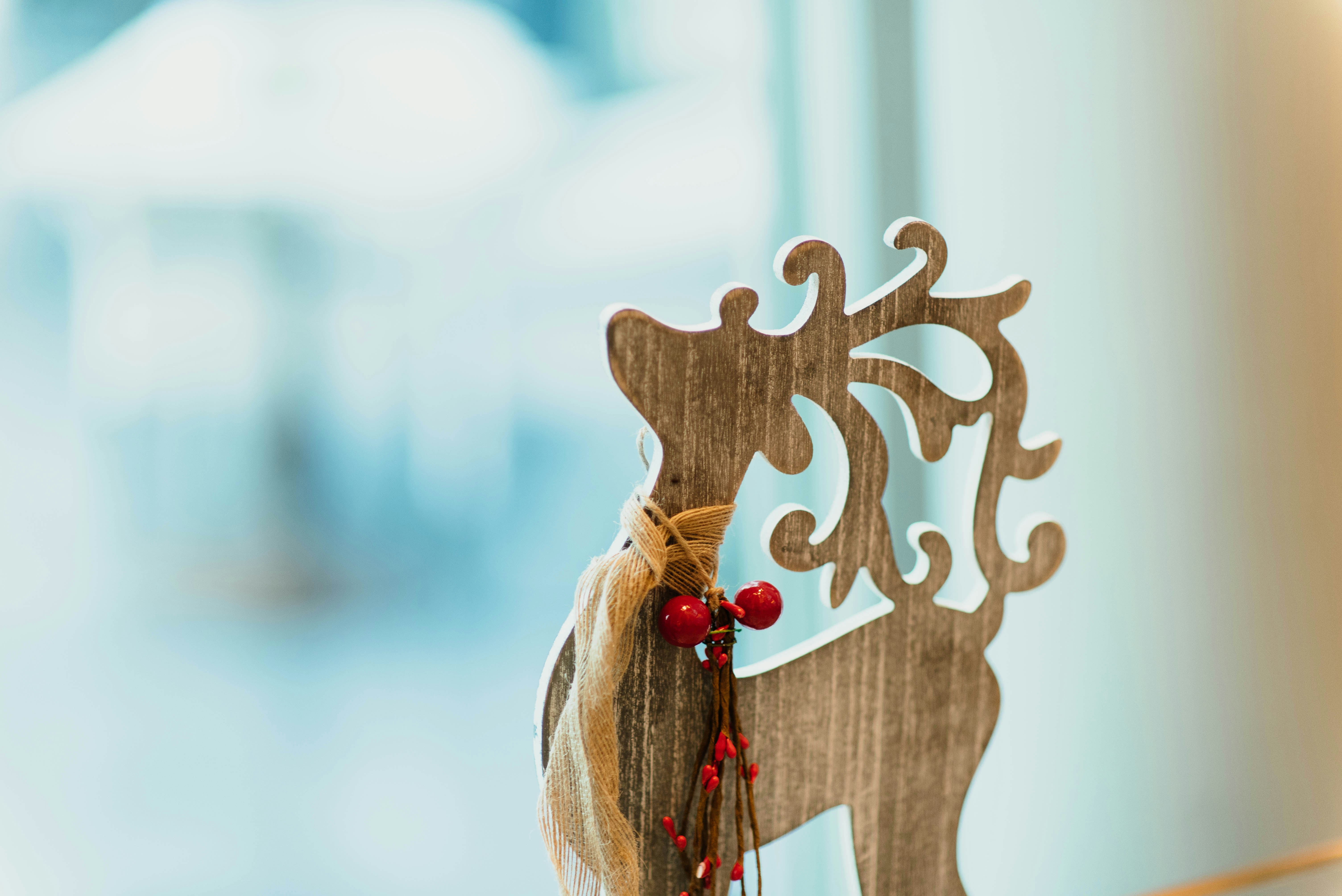 A wooden deer-shaped ornament decorated with red berries and twine against a blurry window background. - wallpaper image