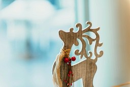 A wooden deer-shaped ornament decorated with red berries and twine against a blurry window background. - wallpaper image