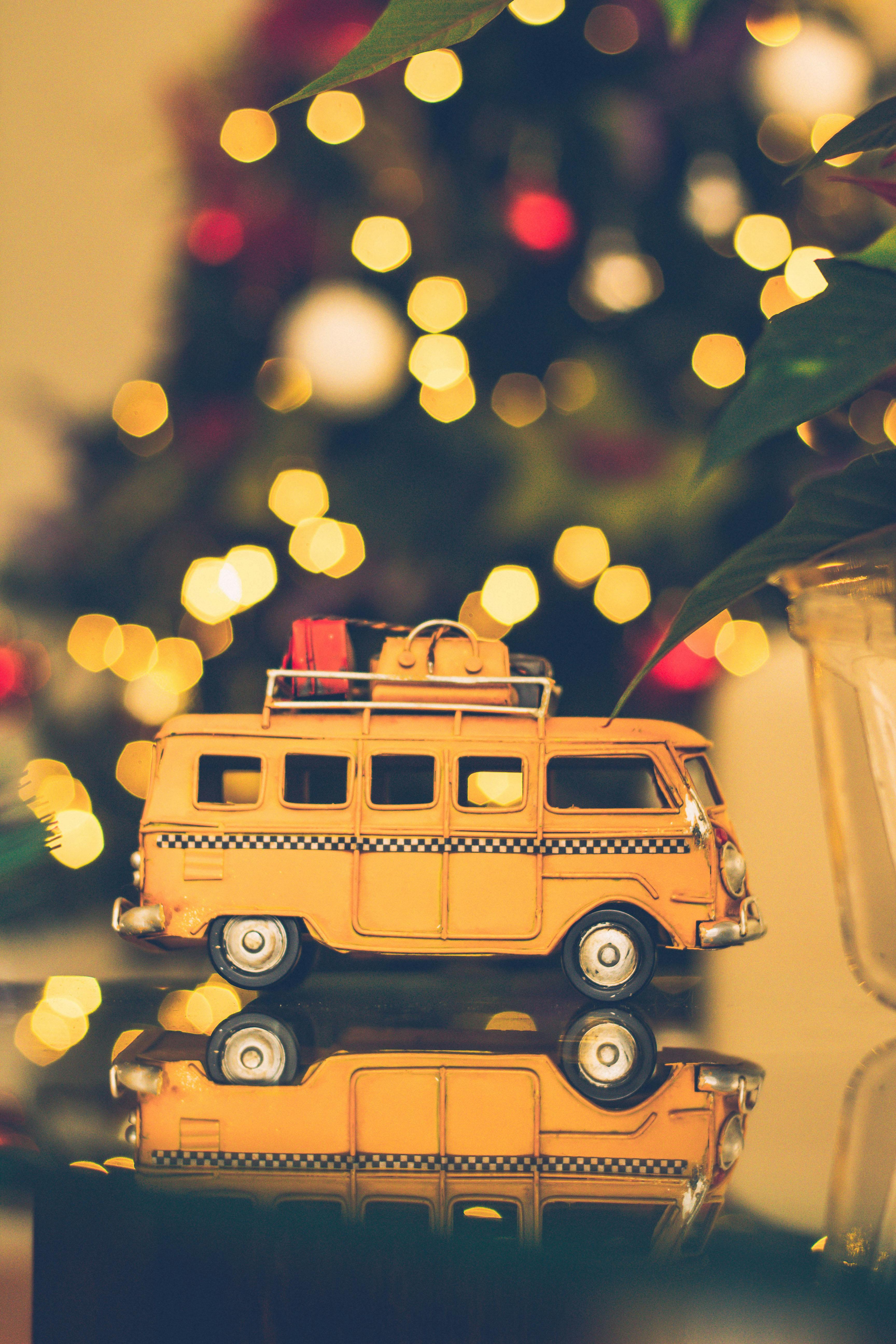 A yellow toy van is on a table with a decorated Christmas tree in the background. - wallpaper image